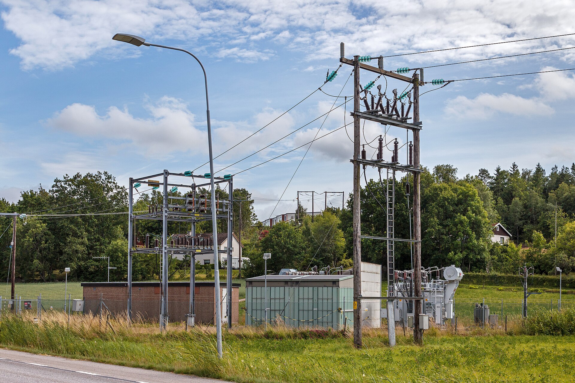 Nätstation med ledningar, isolatorer och transformatorer under en blå himmel.